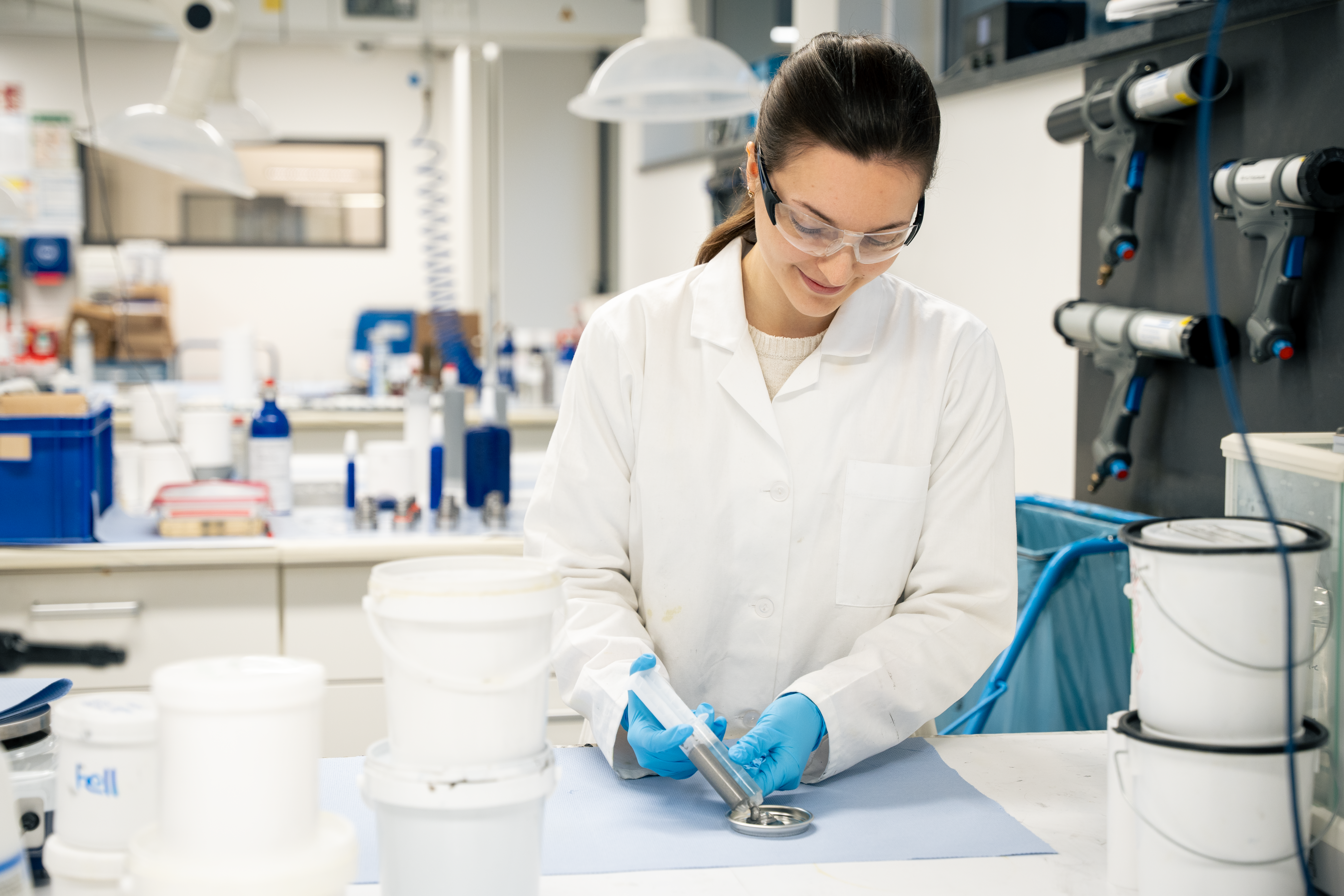 Een vrouw met een witte jas en een veiligheidsbril staat in het laboratorium en plakt iets vast