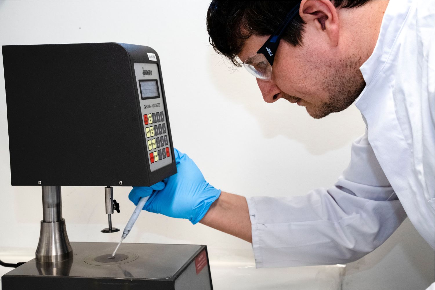 Een man in een witte jas druppelt iets uit een pipet op een oppervlak