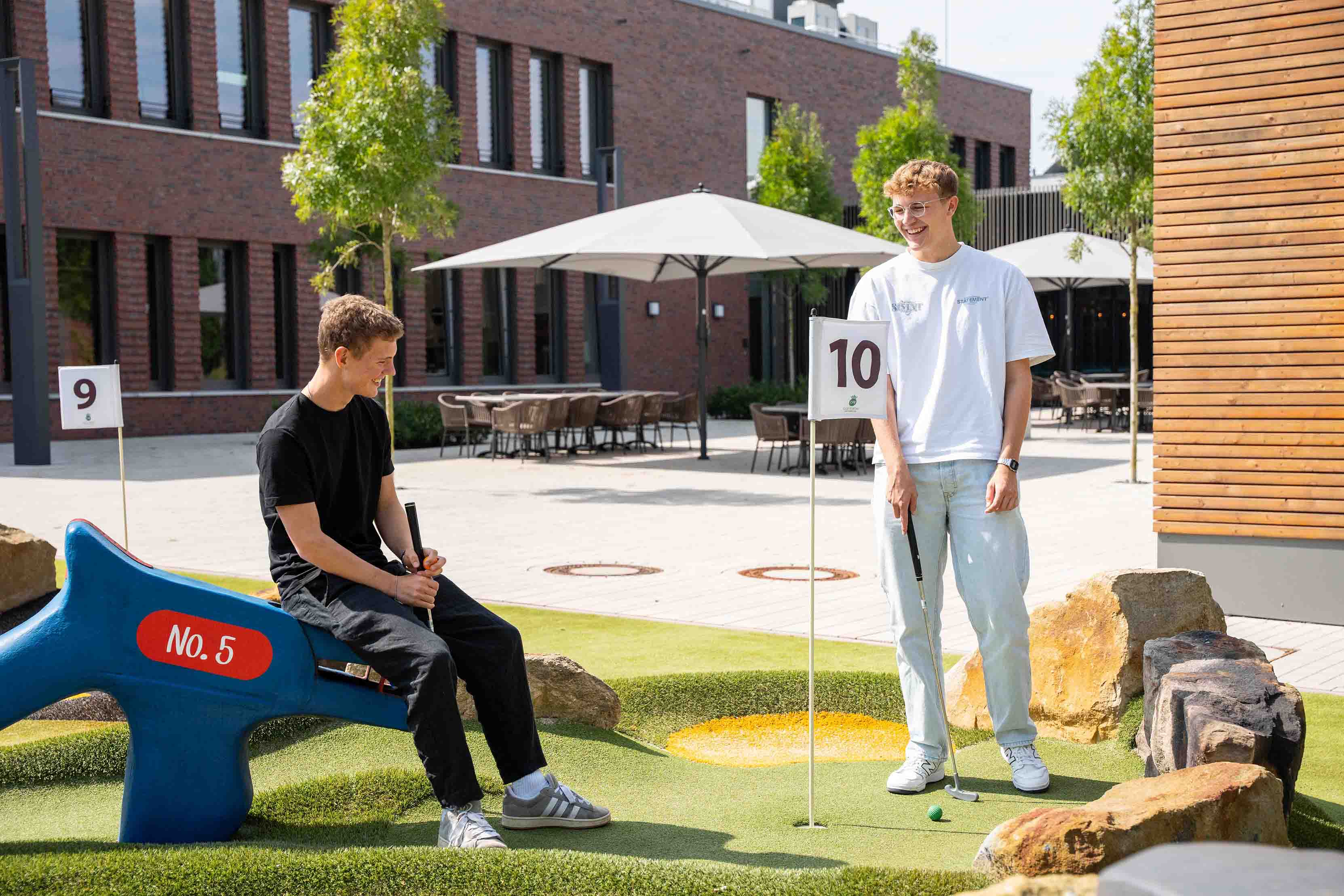 Twee jonge mannen spelen samen minigolf en lachen daarbij.